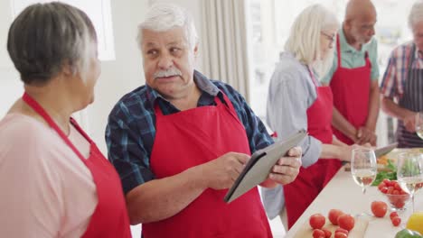 Happy-diverse-senior-male-and-female-friends-using-tablet,-preparing-food-in-kitchen,-slow-motion