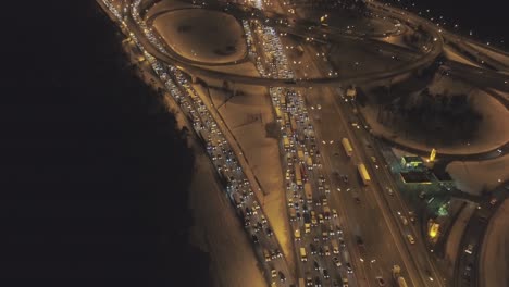 illuminated complex highway junction and cars traffic jam at winter night. drone is flying upward. aerial view. establishing reveal shot.