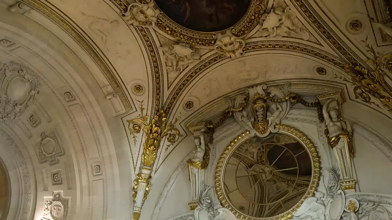 A detailed view of an ornate ceiling with sculptures and visitors in a grand hall.