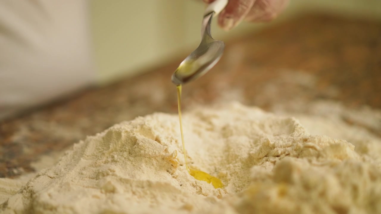 Slow motion close-up of olive oil being drizzled into a flour mixture by a skilled chef, beautiful depiction of rustic cooking techniques and natural ingredients
