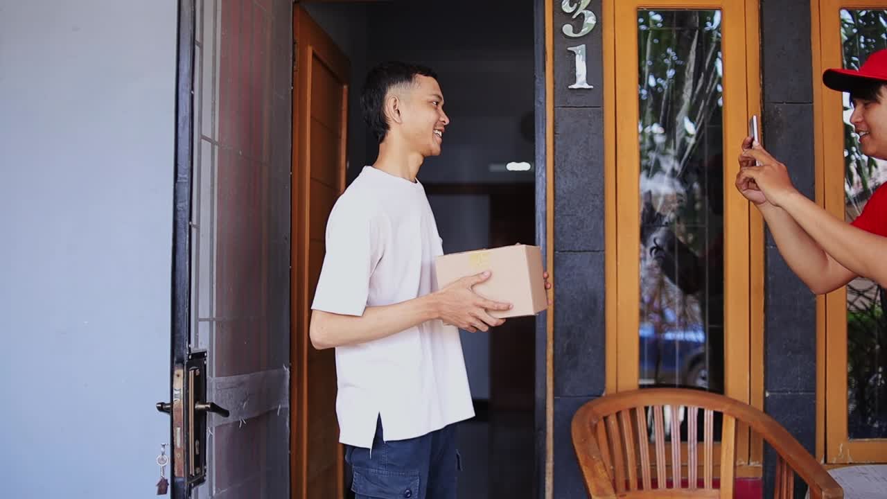 Happy customer receives package from delivery person using phone for confirmation at doorstep
