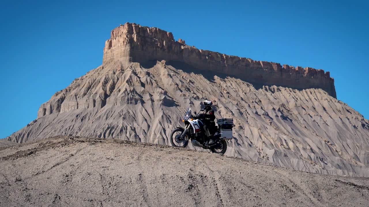 Motorcycle rider on Yamaha Tenere Adventure Bike driving up to cliff overlooking scenic outlook with alien mountain in background in 180 fps slow motion.
