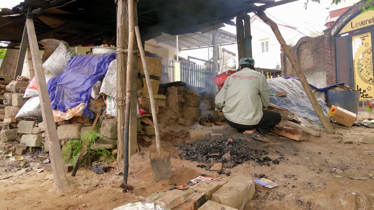 Sudut samping lebar pengrajin tembikar meneteskan bensin untuk menyalakan api di desa Than Ha, Hoi An, Vietnam
