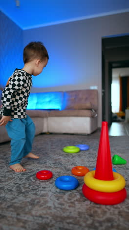 caucasian boy walks by the room picking his toys. cute active toddler building a pyramid. vertical video.
