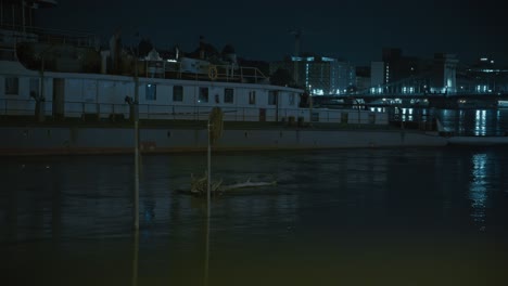 floodwaters submerge a riverside sign with floating debris in budapest at night