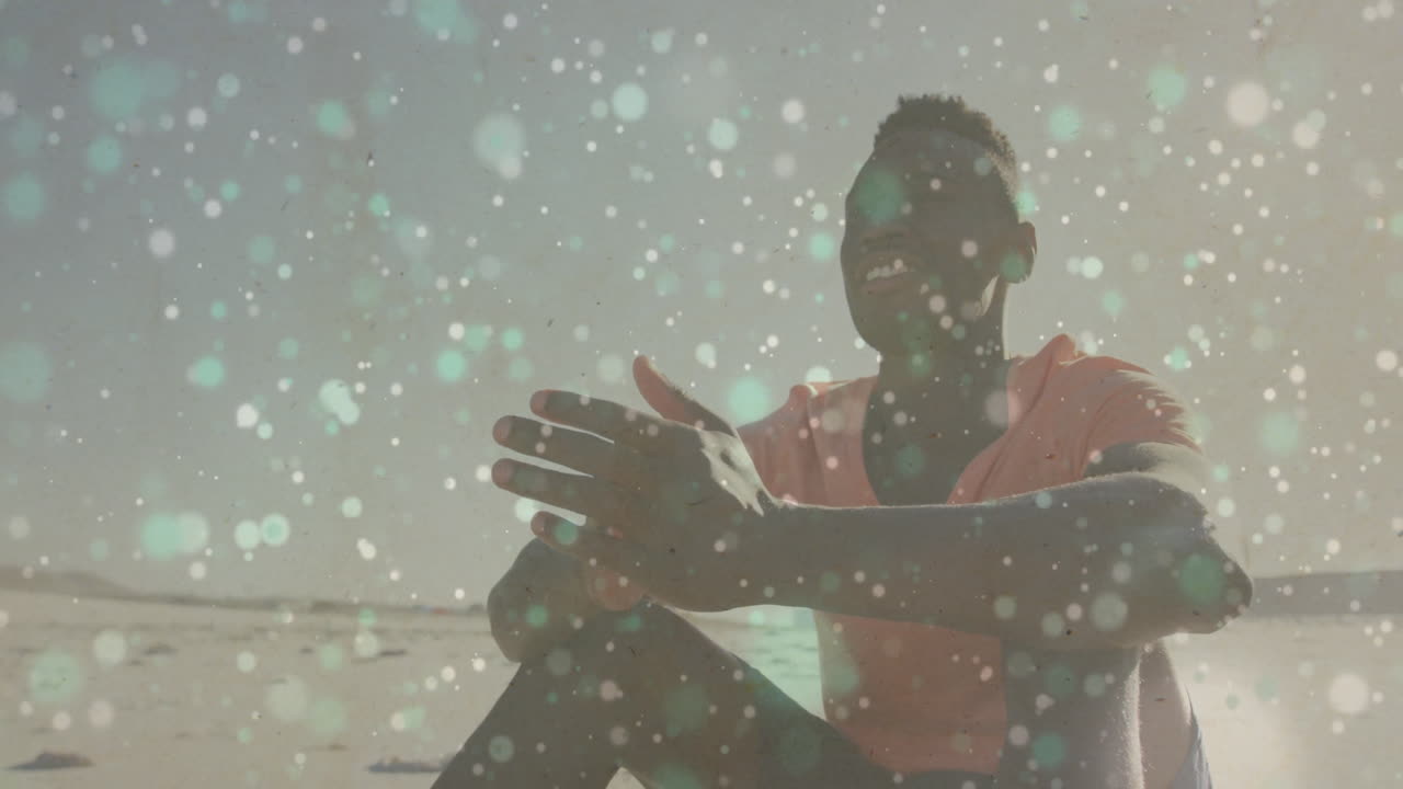 Man sitting cross-legged on beach, showcasing animated bokeh lights for marketing design work