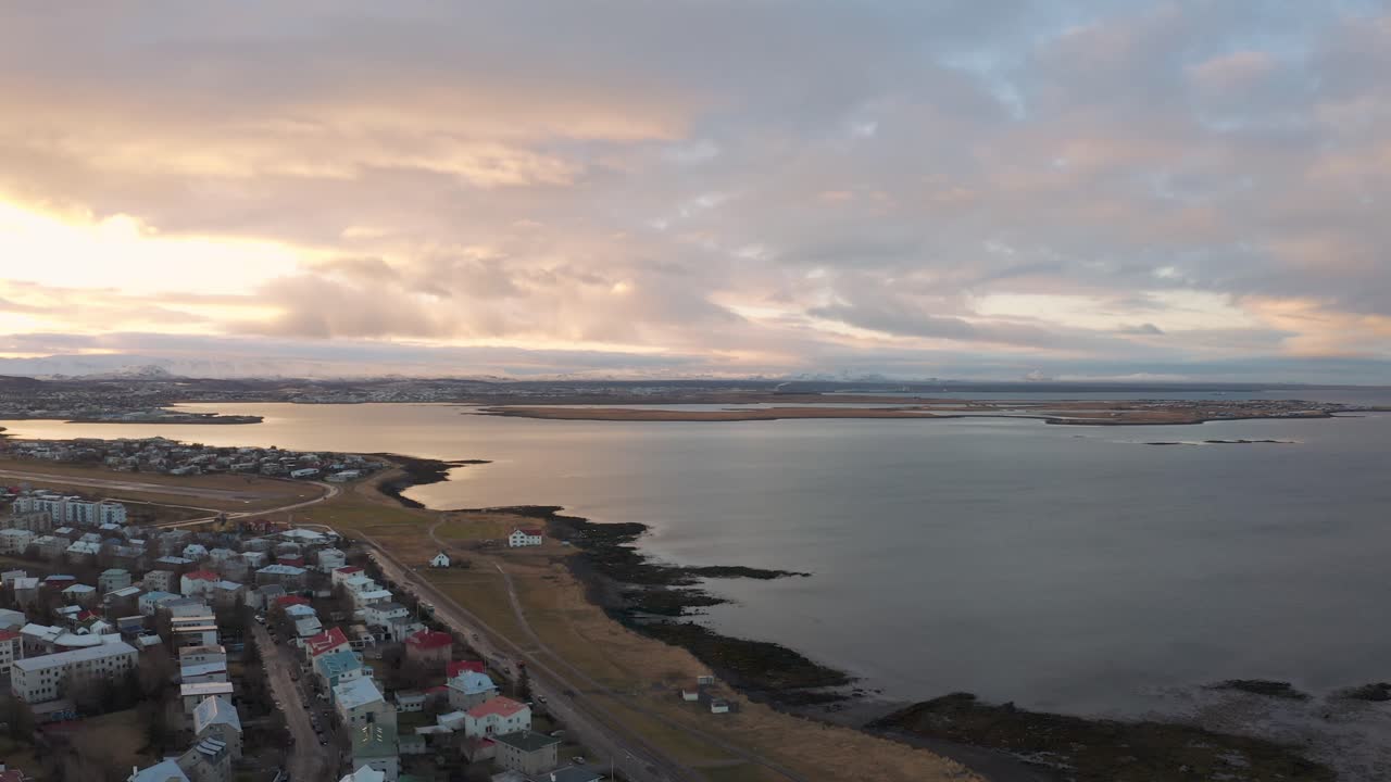 Epic Drone Pullback Over Coastal Residential Reykjavik Houses during a Beautiful Sunset Reflecting off the Ocean, Iceland