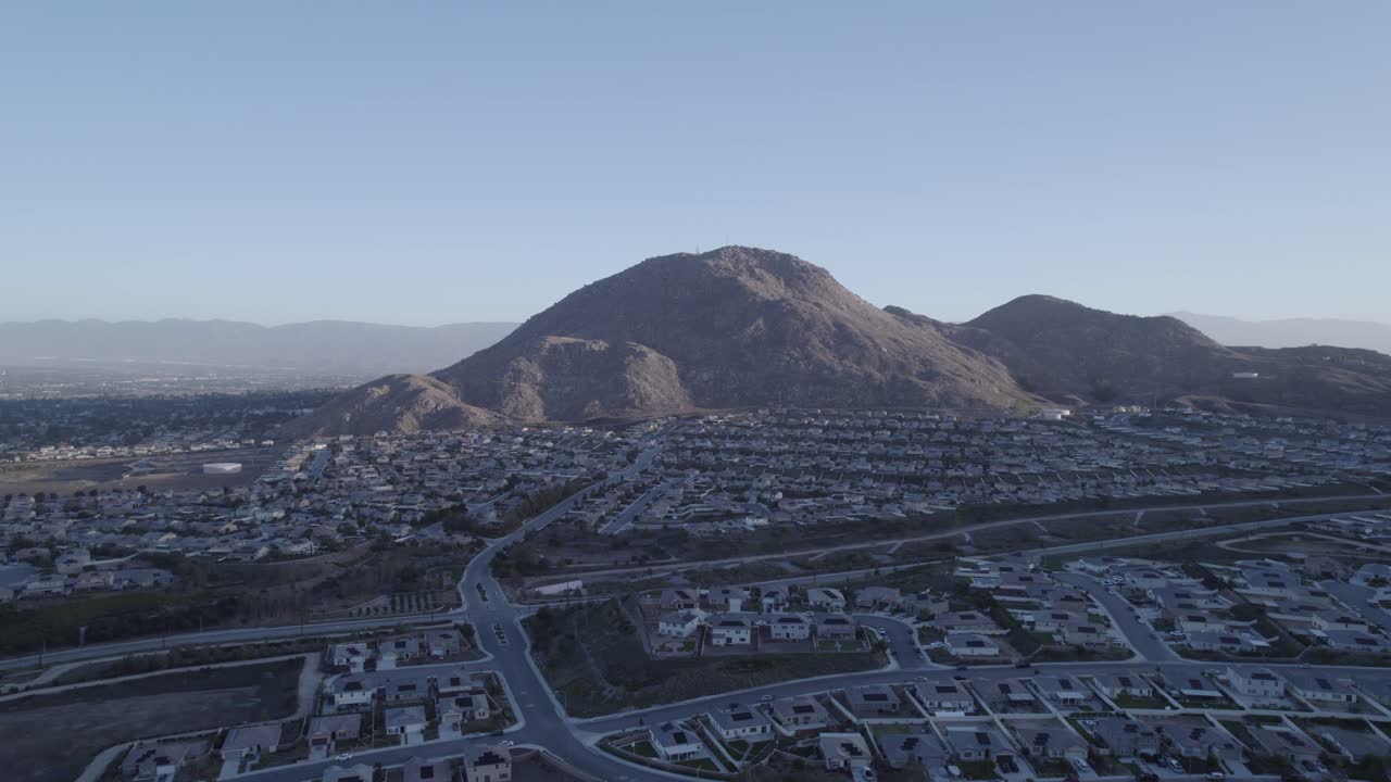 A captivating drone flight enters a neighborhood, highlighting the majestic blue mountains in the background, bathed in the warm morning sun
