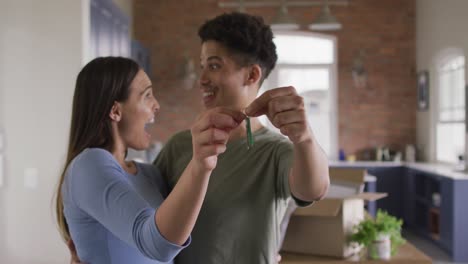 Portrait-of-smiling-biracial-couple-moving-house,-holding-key-and-embracing