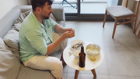 man relaxing at home, pouring and drinking beer with snacks