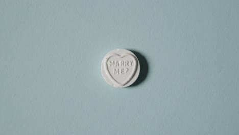 hand picking up heart candy with marry me message on blue background