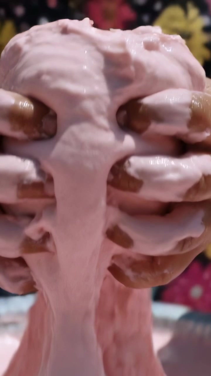 Video verticale: Un bambino curioso con una maglietta rosa preme e allunga dello slime rosa in una ciotola sul tavolo per percepirne la consistenza.