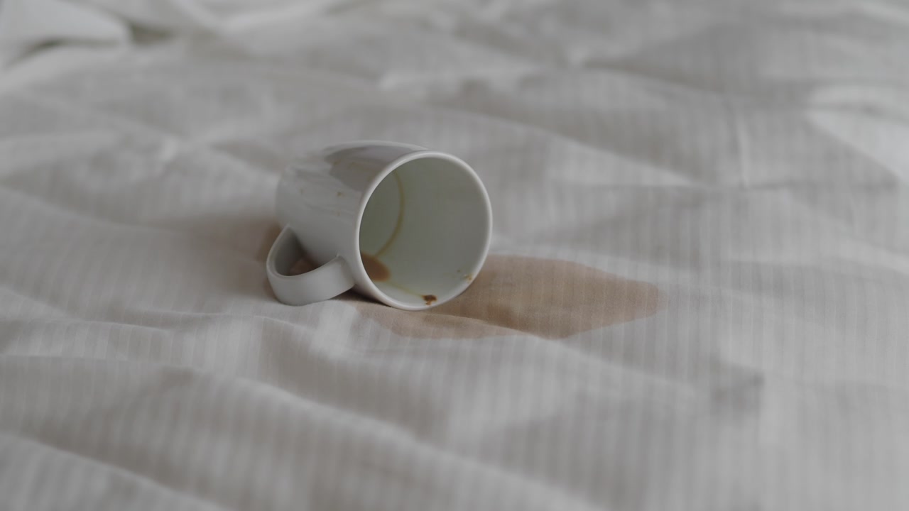 Close-up of a Spilled Coffee Mug and Stain on White Bedsheet