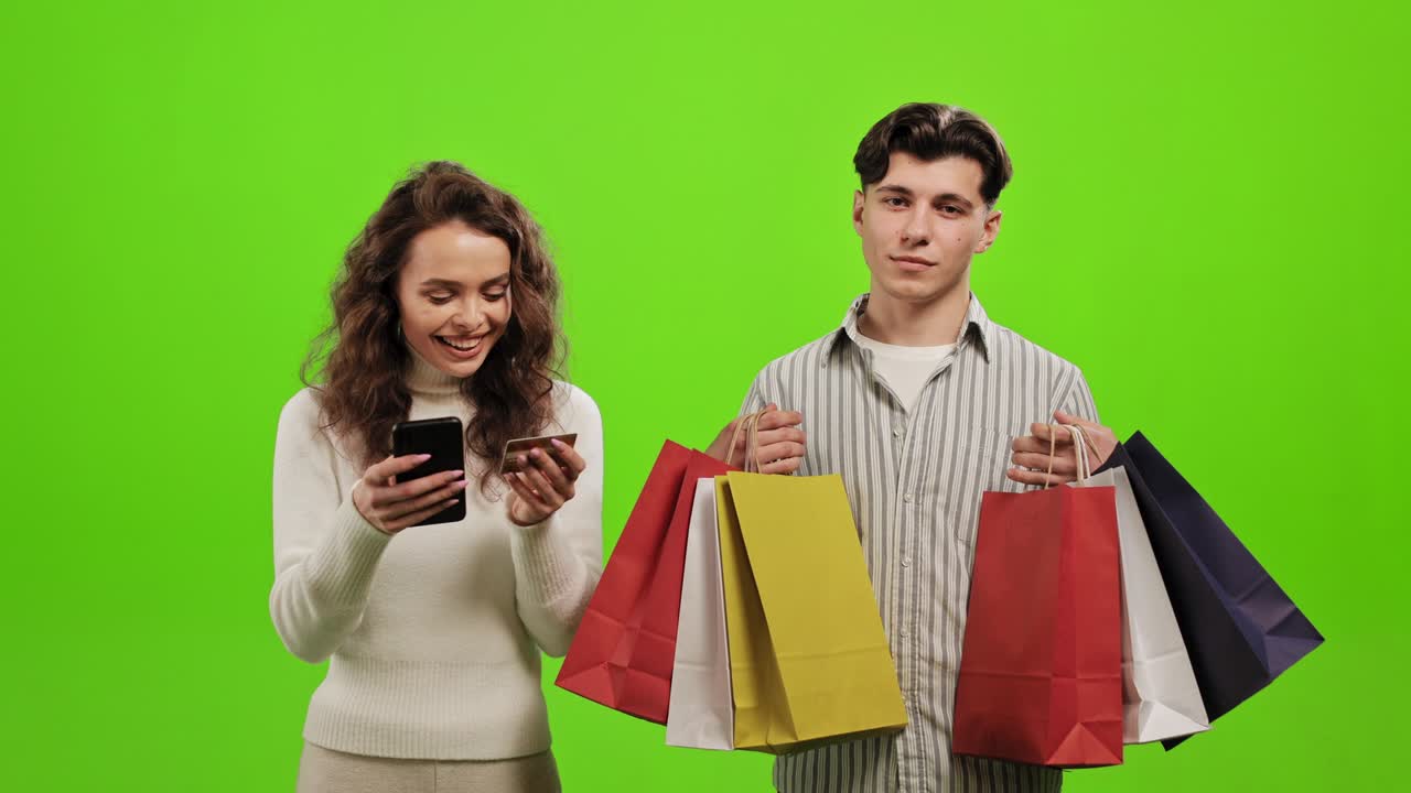 un hombre está sosteniendo bolsas de compras. una mujer está felizmente pagando por comprar en línea. están de pie sobre un fondo verde. pantalla verde. 4k.