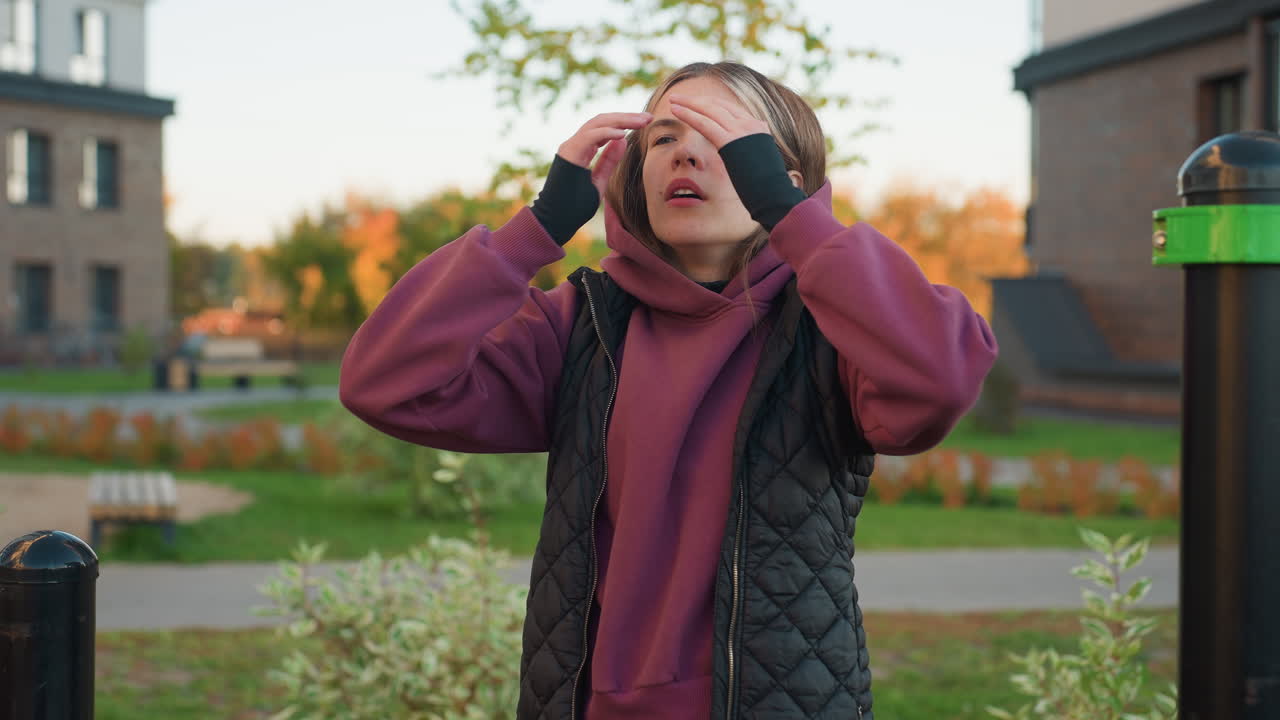 Wellness minded woman flexing her fingers outdoors in an urban park while wearing a hoodie and vest, she is focused on her physical well-being and fitness, practicing mindfulness