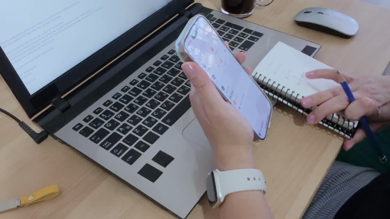 A person is using a laptop and a cell phone. The laptop is open and the cell phone is in their hand.