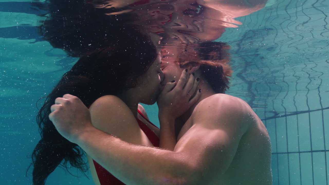 young couple kissing underwater in swimming pool enjoying intimate kiss  romantic lovers submerged in water floating with bubbles in passionate  intimacy