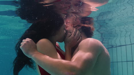 Pareja-Joven-Besándose-Bajo-El-Agua-En-La-Piscina-Disfrutando-De-Un-Beso-íntimo-Amantes-Románticos-Sumergidos-En-Agua-Flotando-Con-Burbujas-En-Una-Intimidad-Apasionada