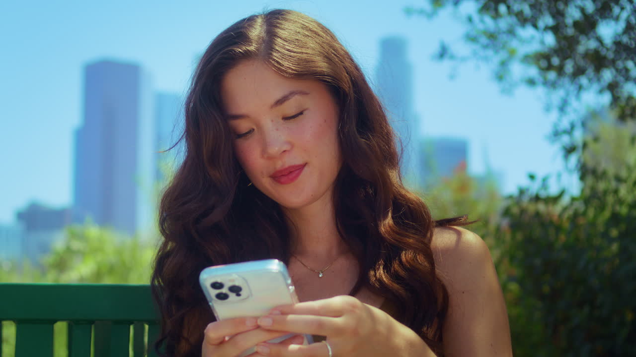 파크에서 전화로 메시지를 입력하는 갈색. 아시아 관광객이 야외에서 가을 사용합니다.