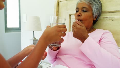 Female-doctor-giving-glass-of-water-to-sick-senior-woman-on-bed-4k