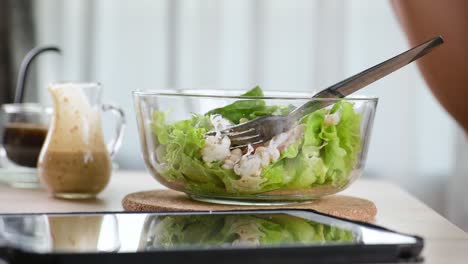 wife serves bowl glass of green vegetable salad to husband at breakfast table at home. eat fresh salad and clean vegetable can eat raw. eat food, drink coffee, see and slide touch screen tablet computer tablet.