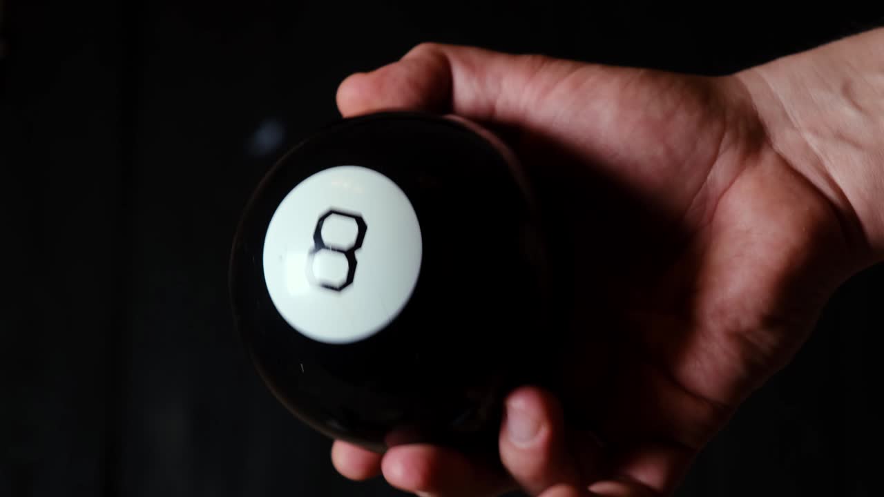 Sfera delle predizioni a forma di otto nella mano di un uomo su sfondo nero.