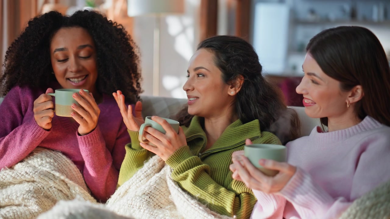 Friends enjoy cozy girly gathering sitting home sofa covered blanket closeup.