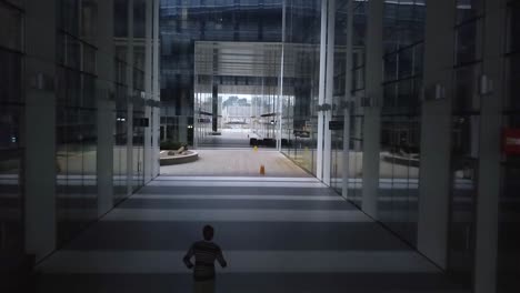 follow aerial shot of a young male in casual clothes as he runs through a deserted business environment