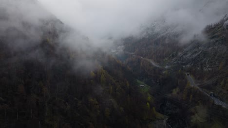 Entspanntes-Vorwärts-Fliegendes-Drohnenvideo-In-Richtung-Wolken-Im-Schweizer-Alpental-An-Einem-Stimmungsvollen-Grauen-Winternachmittag-Mit-üppigen-Kiefernwäldern-Und-Wunderschönen-Schneebedeckten-Bäumen-Auf-Bergen-Mit-Straße-In-Der-Mitte-Des-Tals