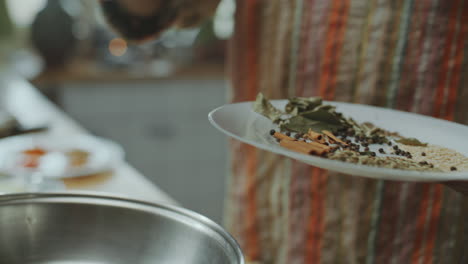 manos del chef añadiendo especias indias a la sartén calentada para cocinar