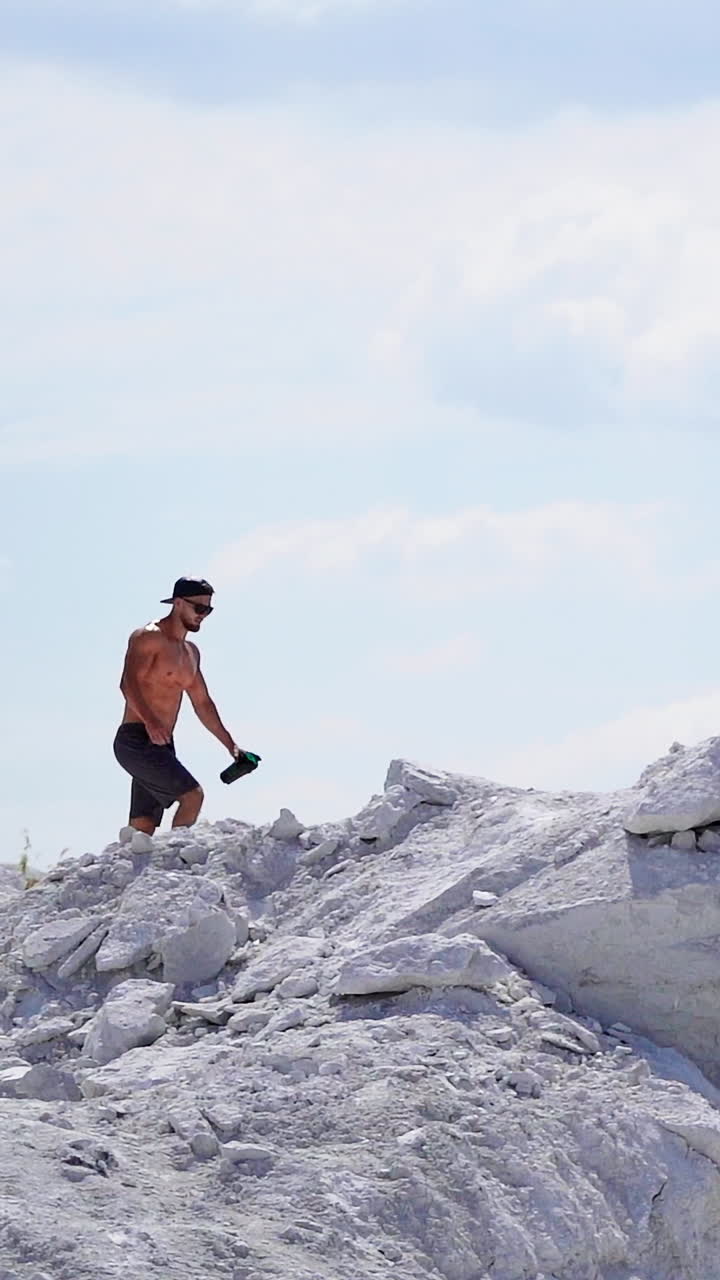 Slow motion of strong athlete in the mountains. Shirtless sportsman walking up the white hill in summer. Muscular man exercises outdoors. Vertical video