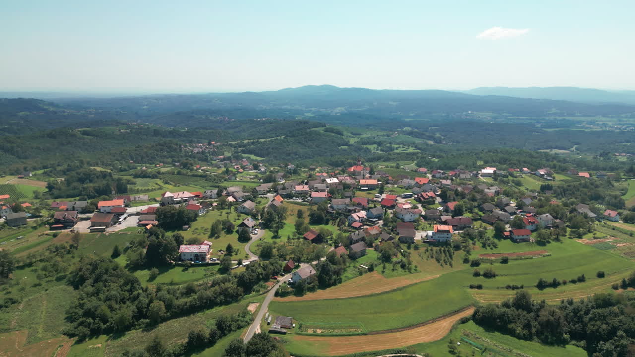 una foto de un pequeño pueblo en eslovenia con colinas y bosques en el fondo