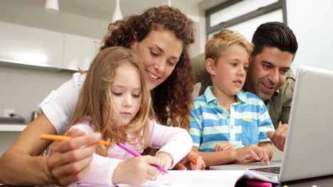 niños felices dibujando en la mesa con sus padres y usando computadora portátil