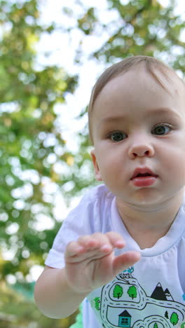 curious little baby boy exploring the camera and clapping by it. low angle view. blurred backdrop. vertical video