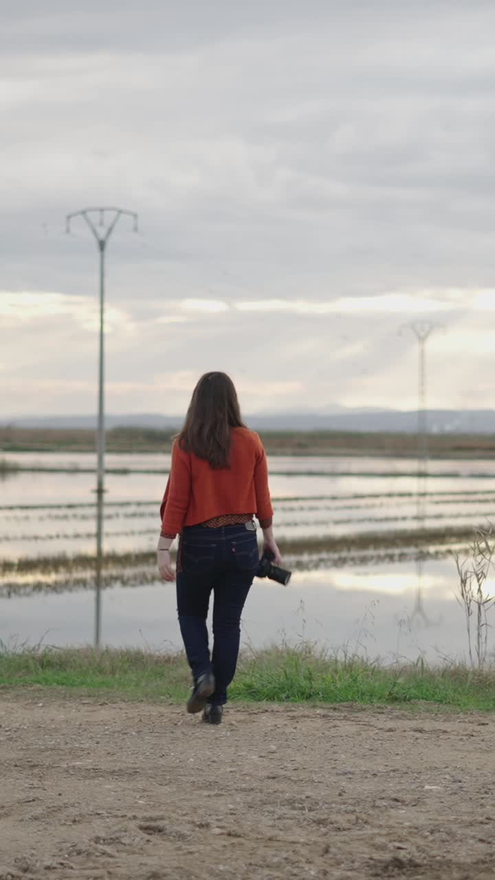 Woman Walking with Camera in Rural Landscape
