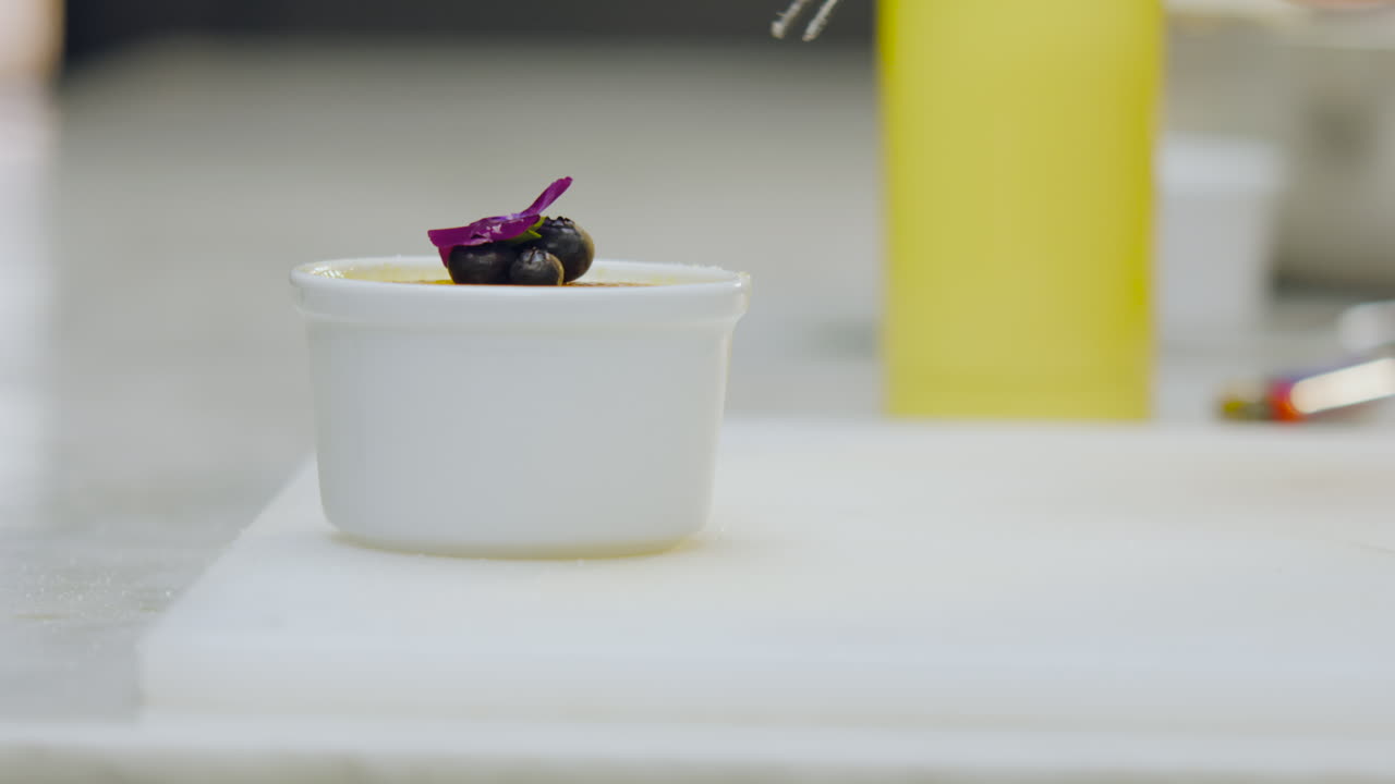 Close-up of a chef adorning a creme brulee with a flower, highlighting the elegant presentation and culinary detail