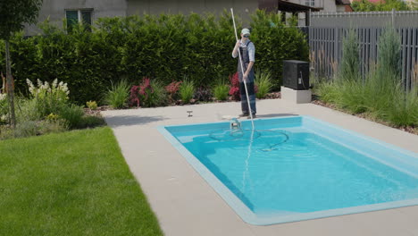 a worker cleans a swimming pool with a special vacuum cleaner.