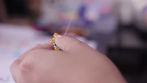primer plano de las manos de la mujer haciendo artesanías con pequeñas cuentas coloridas, aguja e hilo 004