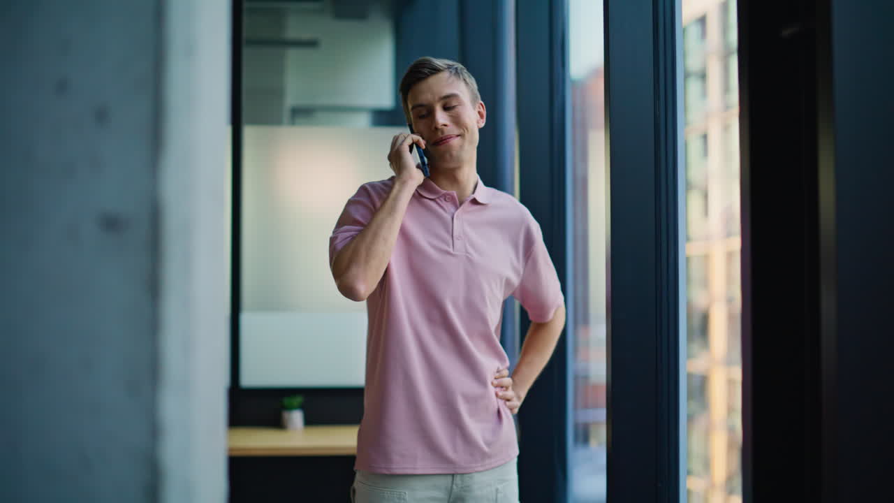 Uomo sorridente che parla al telefono in un ufficio moderno. Ragazzo felice durante una conversazione telefonica