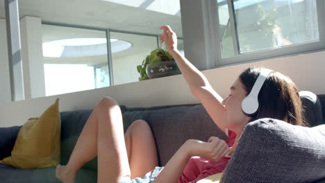 Teenage-Caucasian-girl-enjoys-music-on-a-couch-at-home,-taking-a-selfie-with-her-phone