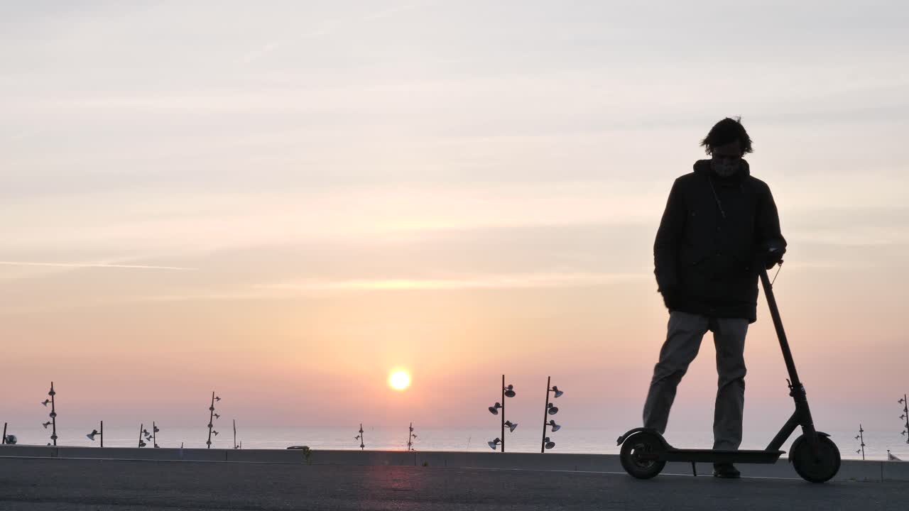 Man wearing face mask walks back to scooter from sunrise landscape and rides off