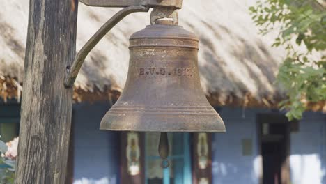 hundred years old copper bell in front of traditional wooden hut with thatched roof