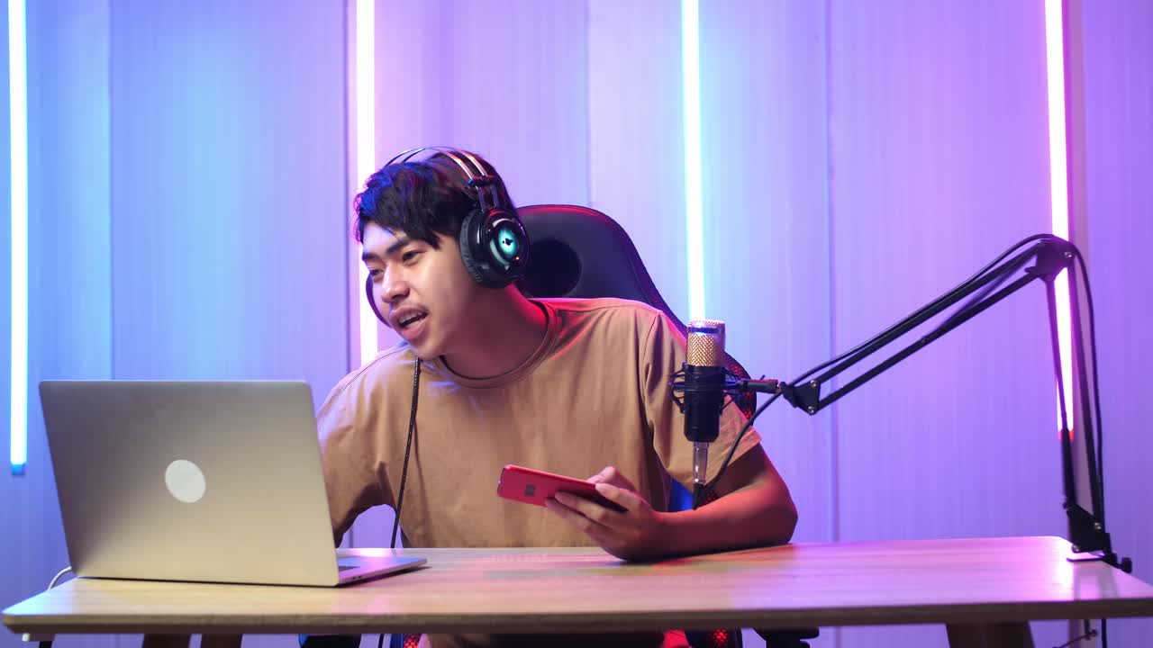 Asian Man Holding Mobile Phone And Read Comment In Laptop Computer Then Talking To Camera While Live Stream