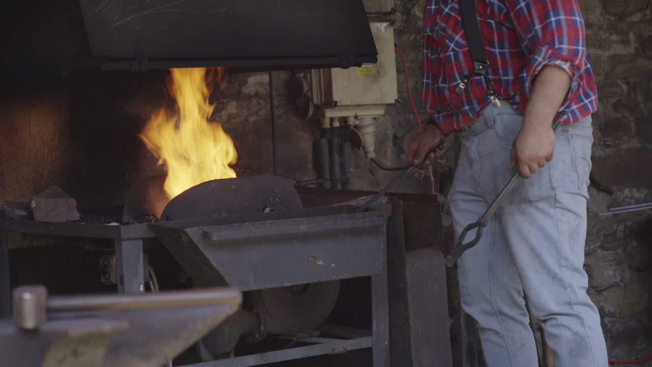 The blacksmith puts coal into the forge with a shovel