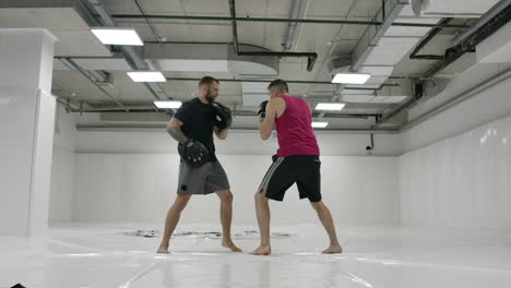 movimiento lento: golpe de poder a la pata de boxeo. fuerte atleta tatuado en ropa deportiva entrenando en las patas de boxes con su pareja