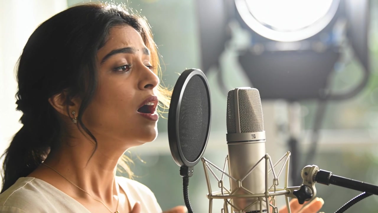 Girandosi verso il microfono a condensatore, cantante indiano che registra la voce in studio con filtro anti-pop e lampada