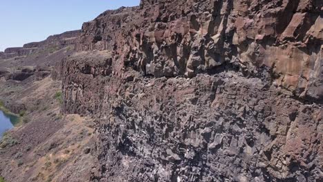 aerial rotates from cliff face to deep blue lake in rugged landscape