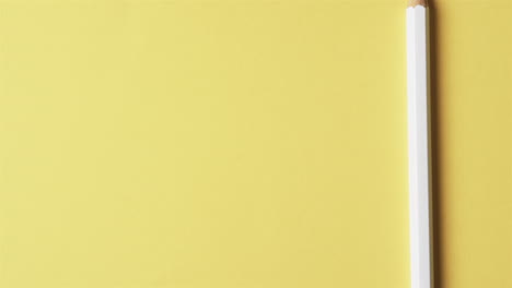 vista aérea de un lápiz blanco con espacio de copia en fondo amarillo, en cámara lenta