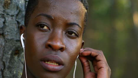 mujer ajustando el auricular contra el árbol 4k