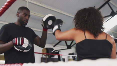 Male-Boxing-Coach-With-Female-Boxer-In-Gym-Using-Training-Gloves-Sparring-In-Ring